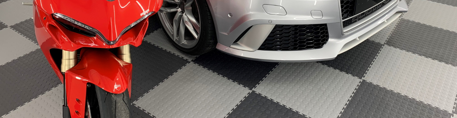 A motorcycle on a floor laid with light grey and graphite interlocking PVC tiles with a raised disk texture.